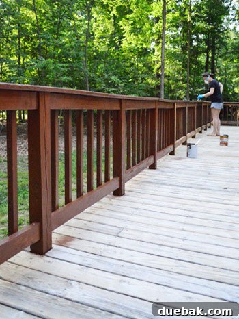 Two people working together to stain the vertical railings of a deck, using brushes for detailed application.