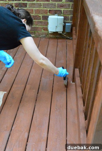 A person meticulously back-brushing fresh deck stain into the wood grain and between boards to ensure even coverage.