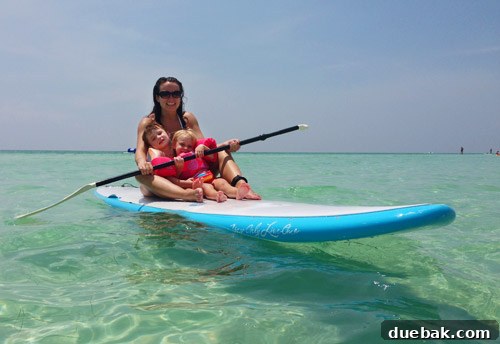 Two children sitting on a paddleboard being ridden by an adult in Destin's calm waters