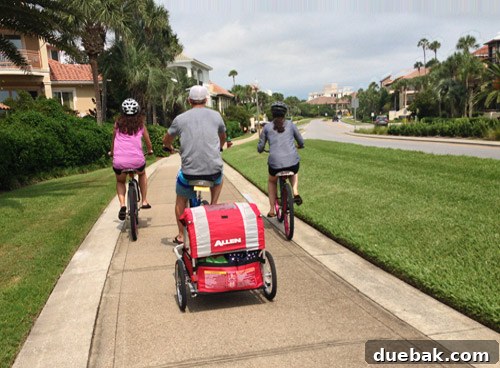 Family biking on a scenic path in Destin, Florida with children in a trailer