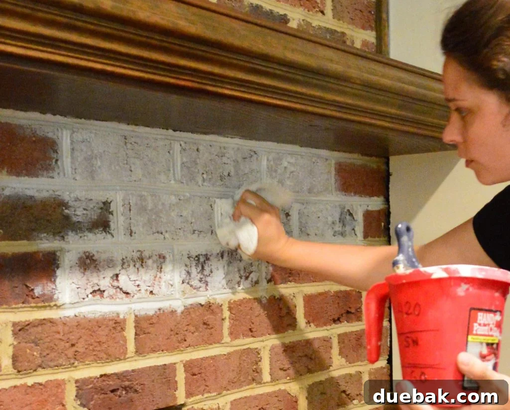 DIY Whitewashing: Transform Your Brick Fireplace 6 Sherry demonstrating the careful dabbing technique with a rag, after applying diluted white paint to a brick wall for a subtle whitewash finish.