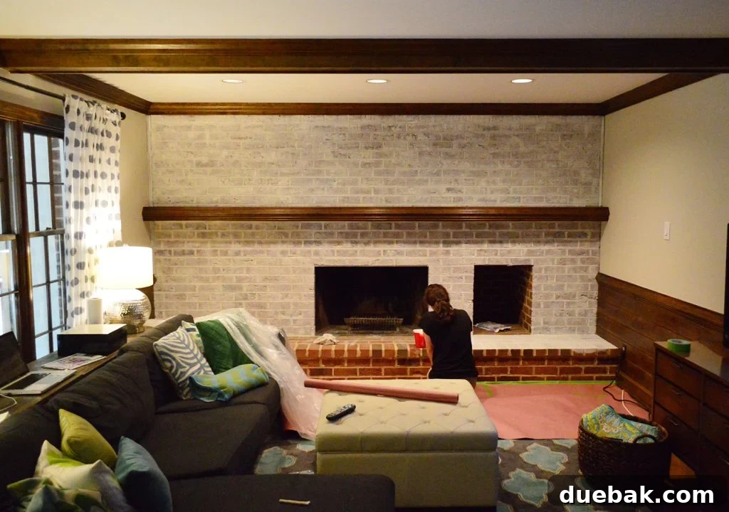 DIY Whitewashing: Transform Your Brick Fireplace 9 A nearly completed first coat of whitewash paint applied to a fireplace brick wall in a dated living room, showing significant transformation.