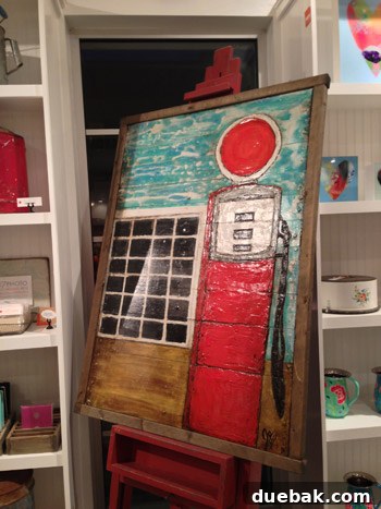 Seaside's Simple Pleasures: Window Shopping The Art of Simple 15 A charming painting of an old gas pump with rustic red and teal colors, framed in wood and displayed on an inspiring red easel.