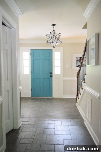 Updated foyer with white trim, fresh paint, a new light fixture, and art, showing the blue stair spindles.