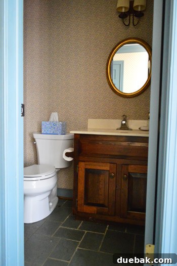 Before shot of the half bathroom, showing old wallpaper and an unpainted vanity.