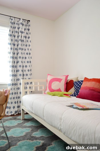 A close-up of Clara's bed with colorful pillows, showcasing the blend of patterns against white furniture.