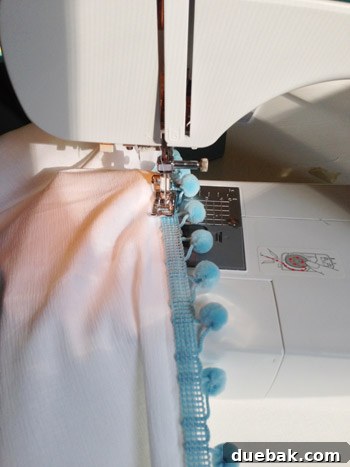 Close-up of pom-pom trim being sewn onto the white fabric