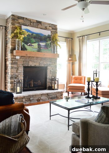 Cozy living room with stone and raw wood fireplace and vibrant orange accent chairs