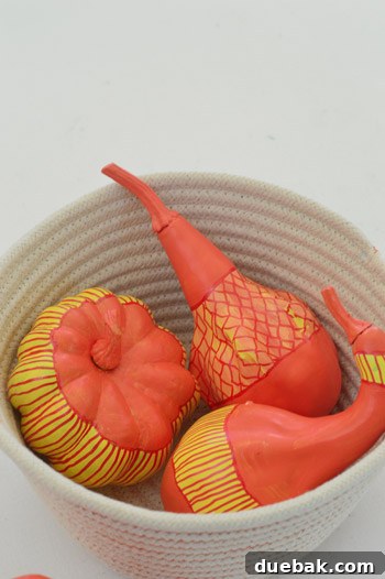 Pumpkins Transformed: The Pantyhose Touch 12 A finished hand-doodled gourd showcasing a yellow band decorated with intricate red triangle patterns, adding unique artistic flair to fall decor.