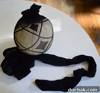 Pumpkins Transformed: The Pantyhose Touch 5 A person's hands carefully fitting a white faux pumpkin into a black fishnet stocking, demonstrating the technique for DIY Halloween decor.