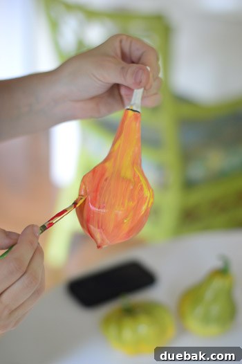 Pumpkins Transformed: The Pantyhose Touch 9 A faux gourd being painted with a blend of yellow and red craft paints, creating a textured orange base, ready for further decoration.