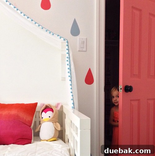 Girl Peeking Out Of Colorful Pink Closet Door Next To Raindrop Mural Bed - A playful shot of a girl peeking out from behind her newly painted, vibrant pink closet door, next to her bed with a colorful raindrop mural.