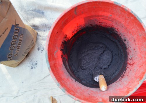 Close-up of mixing charcoal colored grout in a bucket with a hand trowel