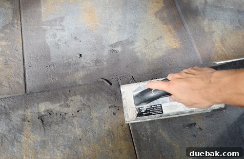 Applying charcoal grout to the tile joints using a grout float, demonstrating the technique
