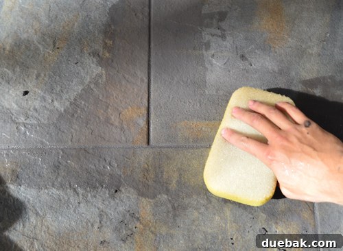 Wiping excess grout from tiles with a damp sponge, shaping the grout lines