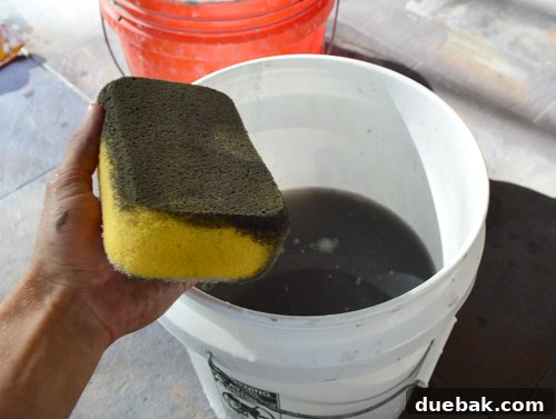Cleaning up excess dark grout from the newly tiled outdoor floor with a sponge