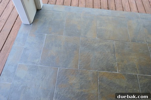 Finished outdoor tiled floor with dark gray grout, showcasing the nearly complete transformation