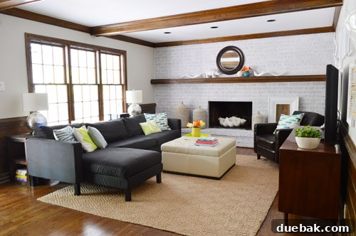 The living room with pink walls, a brick fireplace, and overhead beams, scheduled for a major aesthetic upgrade.