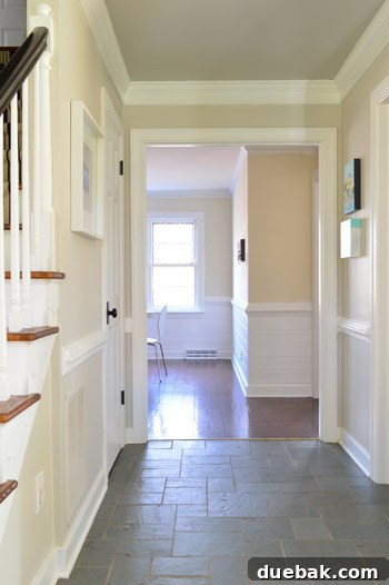 After shot of the bright kitchen view from the front door, with white paneling and a clean aesthetic