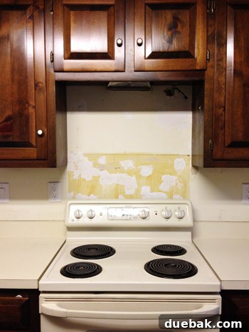 Serene Blue-Gray for Kitchen Walls 10 Wall surface after the old vinyl backsplash has been removed, showing pockmarks and damage that require spackling.