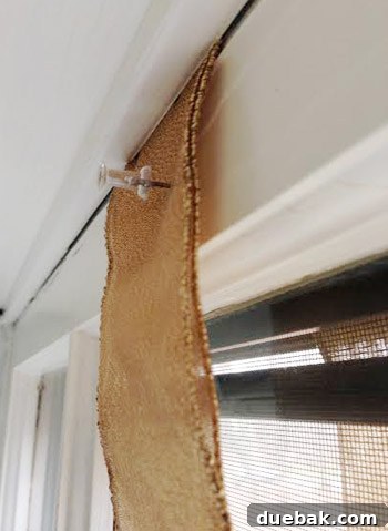 Effortless Window Wreath Styling 8 A beautifully decorated Christmas wreath hanging gracefully from an upstairs window, securely held by a gold ribbon cleverly pinched by the closed window frame and reinforced with a discreet thumbtack.