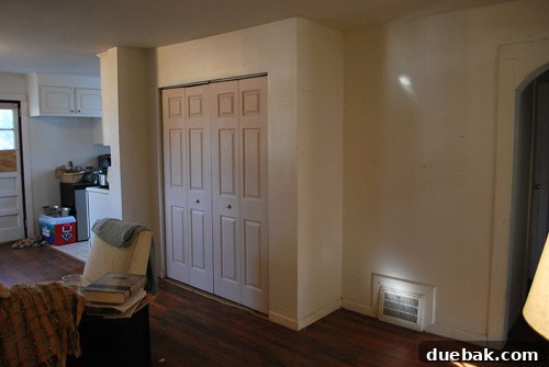 Before photo of the living room, showing an outdated space with a laundry closet.