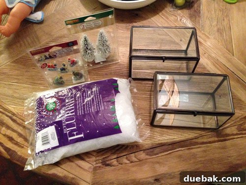 Glass boxes, fake snow, tiny trees, and miniature ceramic dogs laid out as crafting supplies for a holiday project.