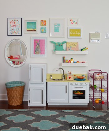 A wider view of Clara's fully decorated play wall, showcasing shelves, artwork, and the mirror in a cohesive arrangement.