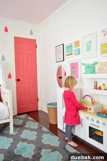 Clara, a young child, standing by her play wall, reaching for a shelf and looking at herself in the mirror, demonstrating scale.