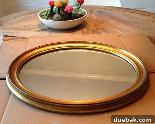 A mirror frame being wiped down with liquid deglosser on a piece of cardboard, preparing it for painting.