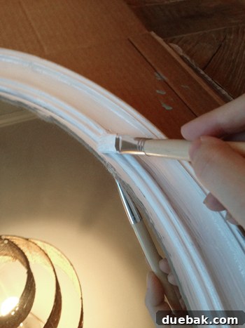 A mirror frame painted white, with some paint specks on the glass, illustrating the first coat of paint.