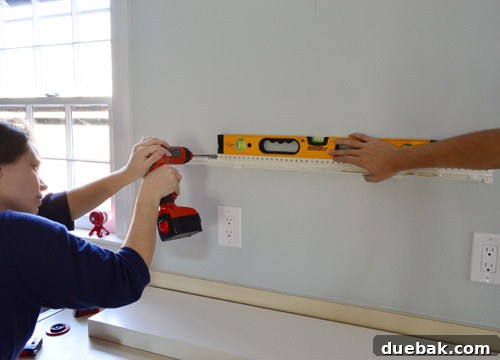 Ensuring the IKEA floating shelf hanging bracket is perfectly level while securely screwing it to the kitchen wall, a critical step for stability.