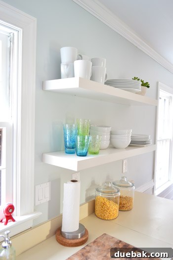 Two long IKEA floating shelves in a kitchen, artfully arranged with vibrant colorful cups and neat stacks of white dishware, showcasing practical and decorative storage.