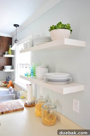 Two pairs of white IKEA LACK shelves elegantly hung in a bright kitchen, adorned with white plates, bowls, and colorful cups, reflecting a minimalist yet functional style.