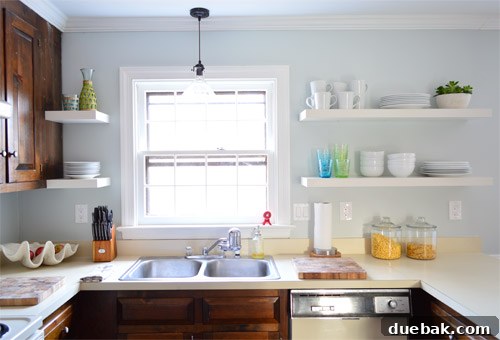 After photo of an updated kitchen showcasing elegant white IKEA floating shelves, demonstrating a significant improvement in brightness and modern aesthetic.