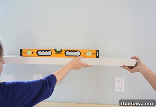 Using a level to precisely mark the placement of IKEA floating shelves on the kitchen wall, ensuring a perfectly straight installation.
