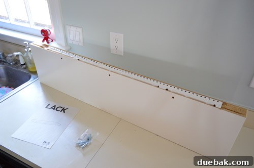 A long IKEA LACK floating shelf, prepared for installation in a kitchen, with its durable metal hanging hardware rail clearly visible.