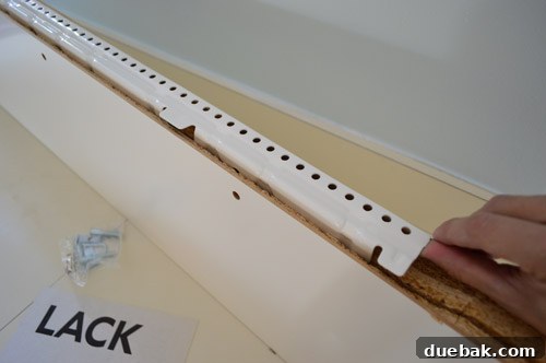 A detailed close-up of the white metal hanging bracket for an IKEA LACK floating shelf, highlighting its sturdy construction and multiple screw holes for secure attachment.