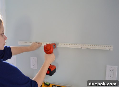 Attaching the metal hanging bracket for an IKEA floating shelf to the kitchen wall using a drill driver, ensuring proper alignment and initial fastening.