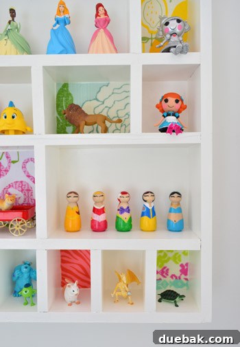 A close-up of a child's hand arranging various small toy figures, including princesses and animals, within the compartments of the cubby shelf.