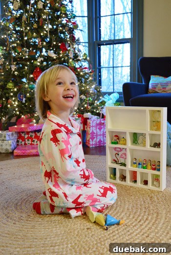 Clara smiling brightly, sitting next to her custom-made white cubby shelf, showcasing her favorite figurines.