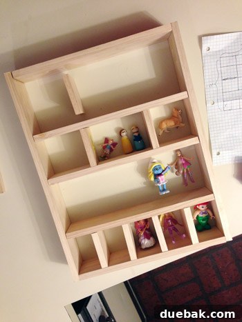 Various small toy figures, including a dinosaur and a peg doll, placed within the partially assembled wooden cubby shelves to check for fit.