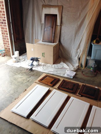 Effortlessly Transform Your Kitchen with White Upper Cabinets 10 Cabinet doors being primed with a paint sprayer in the garage.