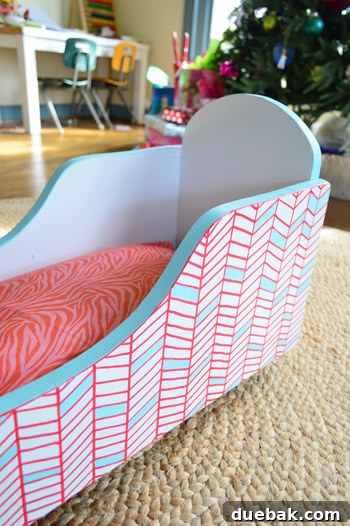 The newly painted cradle with a solid blue top lip and a recovered pink zebra print pillow inside.