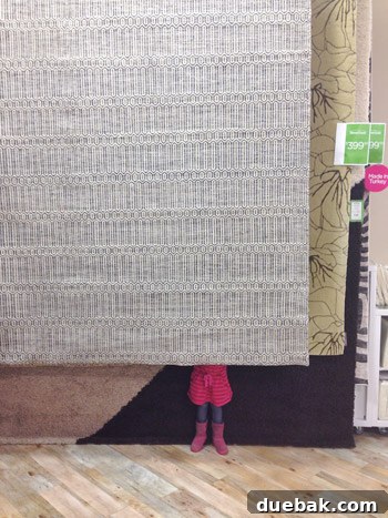 Clara, a young girl, sitting on the large wool rug in HomeGoods, smiling playfully
