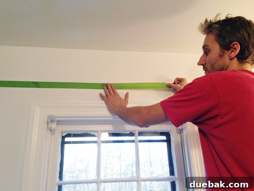 Bathroom Ceiling Transformation with Paint and Trimwork 4 Applying painter's tape along a leveled pencil line in the bathroom for a precise paint border.