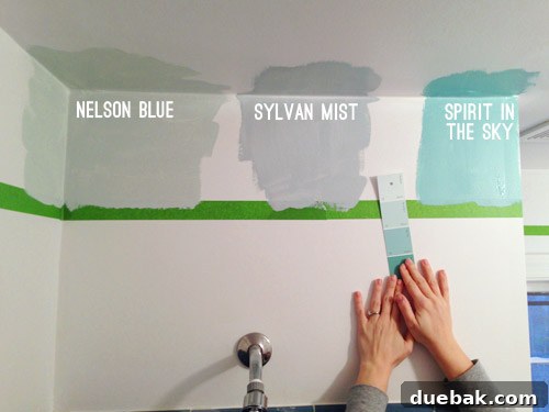 Bathroom Ceiling Transformation with Paint and Trimwork 5 Sherry holding a paint swatch of Spring Mint, comparing it to other blue test swatches on the wall.