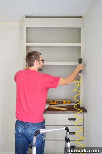 Craft Your Own Library Haven 14 A person expertly nailing trim pieces onto the face of a DIY bookshelf, creating a finished and professional appearance.