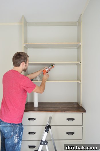 Craft Your Own Library Haven 15 A person meticulously caulking under a shelf of a built-in bookshelf, smoothing seams for a flawless finish.