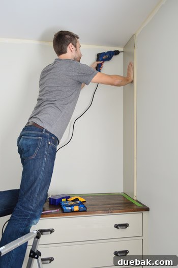 Craft Your Own Library Haven 8 A person securely attaching the side panel of a partially constructed DIY bookshelf to a wall using a drill, ensuring proper alignment.